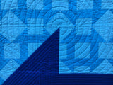 Detail of Minimalist Churn Dash quilt, showing a closeup of one of the dark blue corners with light/medium blue blocks in the background, and concentric circle quilting.